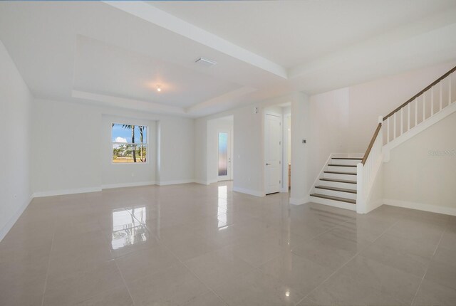 spare room with baseboards, stairway, and a raised ceiling