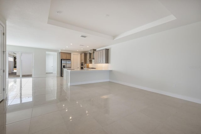 unfurnished living room featuring baseboards, visible vents, and a raised ceiling