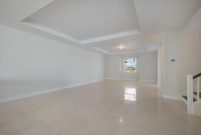 unfurnished room with a raised ceiling, light tile patterned floors, baseboards, and stairs