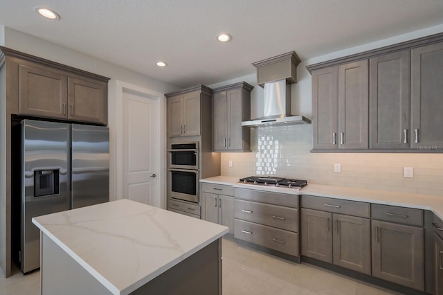 kitchen featuring backsplash, a kitchen island, light stone counters, wall chimney range hood, and appliances with stainless steel finishes