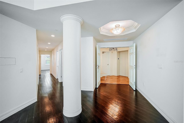 empty room with a raised ceiling, an inviting chandelier, dark wood-type flooring, and ornate columns