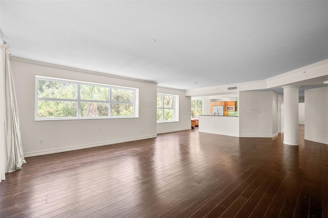 unfurnished living room featuring decorative columns, dark wood-type flooring, and a wealth of natural light