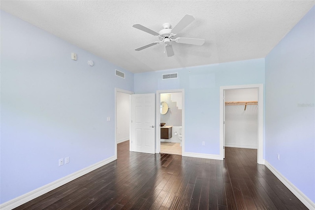 unfurnished bedroom featuring a closet, a walk in closet, dark wood-type flooring, and ceiling fan