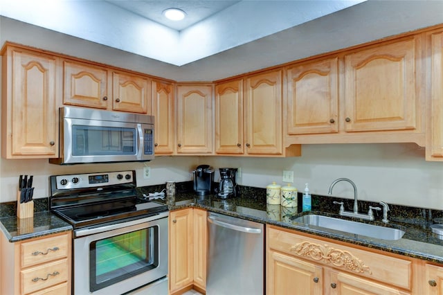 kitchen featuring stainless steel appliances, light brown cabinetry, sink, and dark stone counters