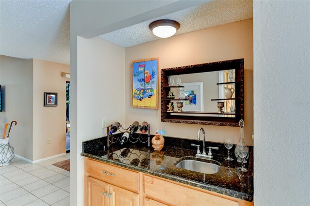 bar with sink, dark stone countertops, a textured ceiling, light tile patterned flooring, and light brown cabinets