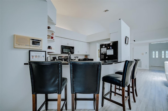 kitchen featuring kitchen peninsula, a breakfast bar, light hardwood / wood-style floors, white cabinets, and fridge