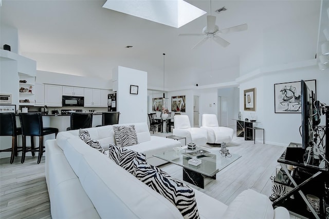 living room featuring high vaulted ceiling, ceiling fan, a skylight, and light hardwood / wood-style flooring