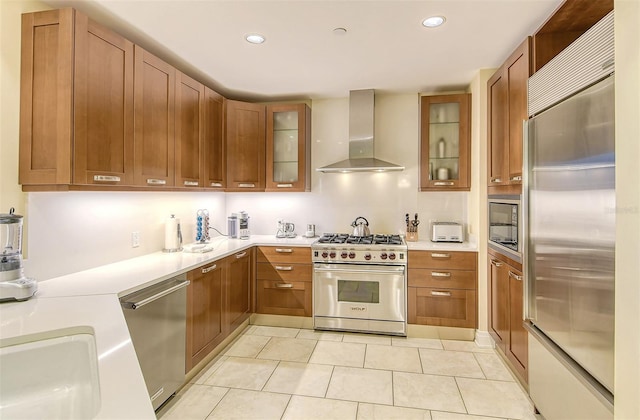 kitchen featuring light tile flooring, built in appliances, sink, and wall chimney range hood