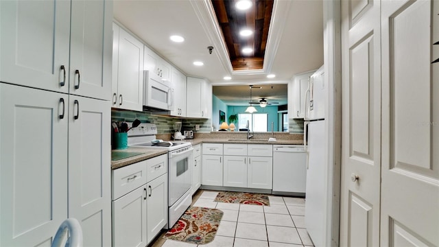 kitchen with white appliances, white cabinets, backsplash, and a raised ceiling