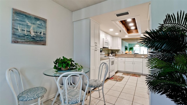 kitchen with white appliances, pendant lighting, light tile floors, a raised ceiling, and white cabinetry