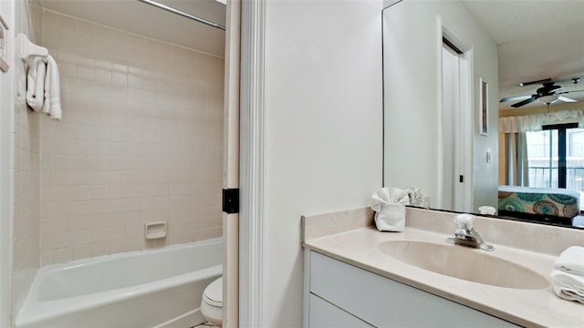 full bathroom with tiled shower / bath combo, toilet, ceiling fan, a textured ceiling, and large vanity