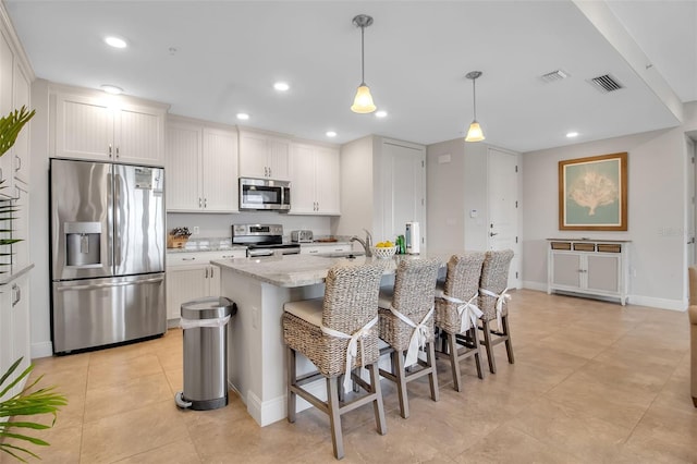 kitchen featuring light stone countertops, stainless steel appliances, an island with sink, decorative light fixtures, and white cabinets