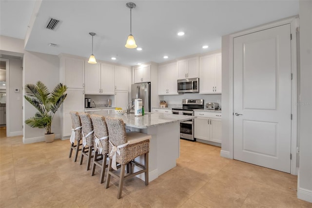 kitchen with a breakfast bar, hanging light fixtures, an island with sink, appliances with stainless steel finishes, and white cabinetry