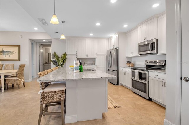 kitchen with a kitchen bar, stainless steel appliances, a kitchen island with sink, white cabinetry, and hanging light fixtures