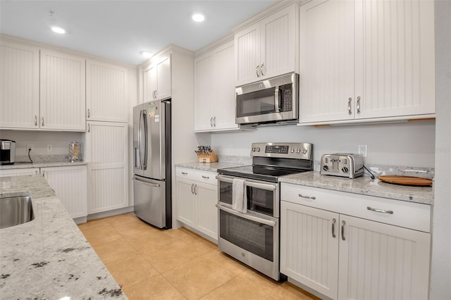 kitchen with light stone countertops, stainless steel appliances, sink, white cabinets, and light tile patterned flooring