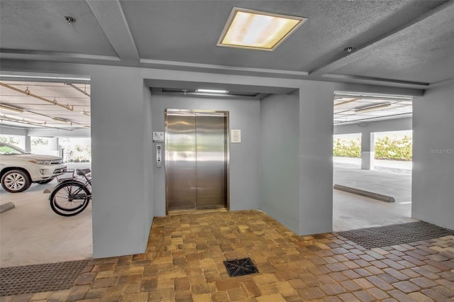 interior space featuring beam ceiling, elevator, and a textured ceiling