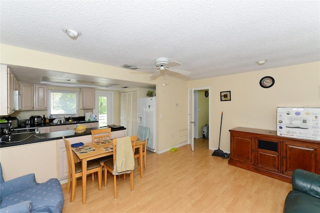 interior space with stove, ceiling fan, white refrigerator with ice dispenser, light hardwood / wood-style floors, and a textured ceiling