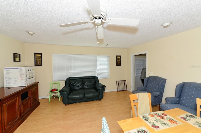 living room with a textured ceiling, ceiling fan, and light hardwood / wood-style flooring