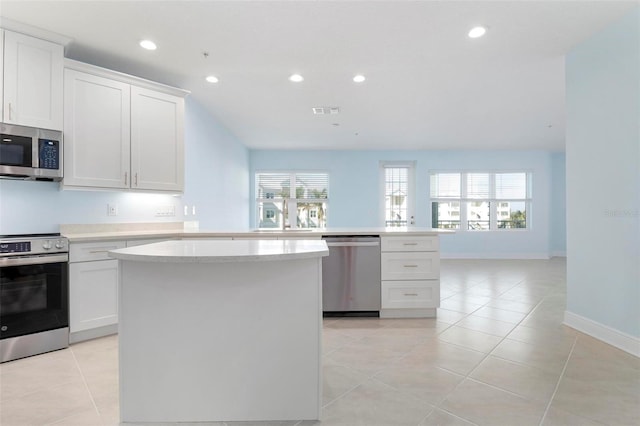 kitchen with kitchen peninsula, appliances with stainless steel finishes, a kitchen island, light tile patterned floors, and white cabinetry