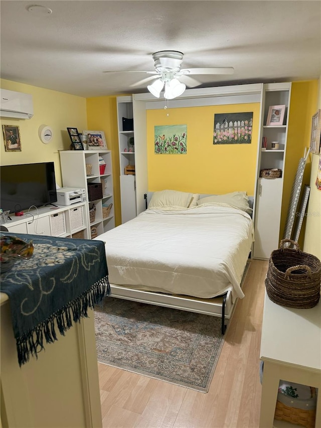 bedroom featuring a wall unit AC, ceiling fan, and light wood-type flooring