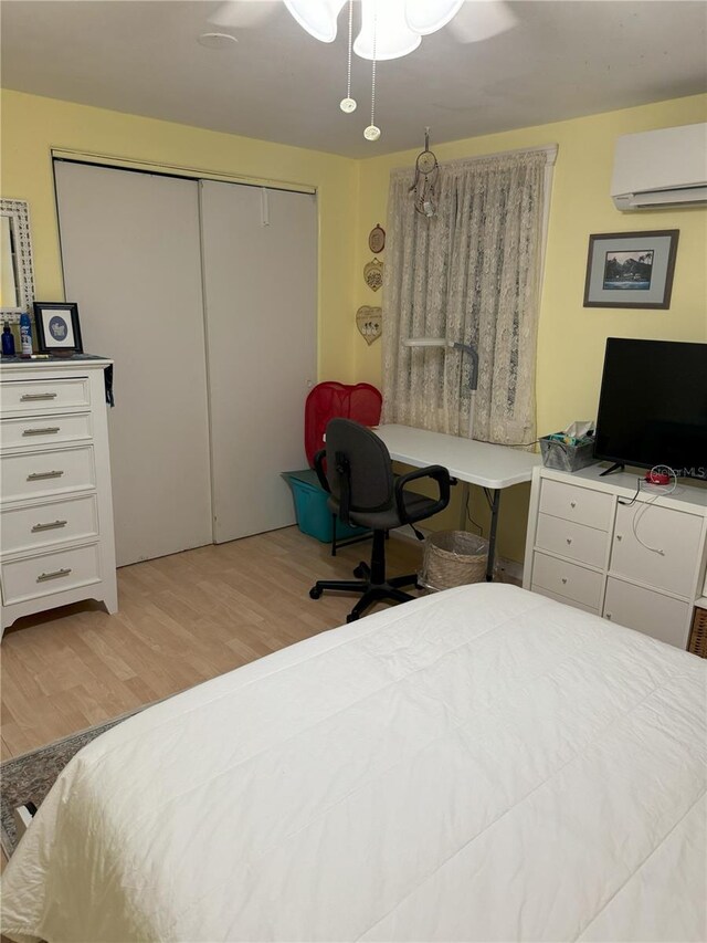 bedroom featuring light wood-type flooring, a closet, an AC wall unit, and ceiling fan