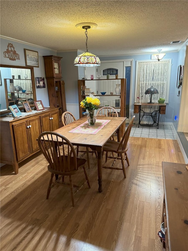 dining room with ornamental molding, a textured ceiling, and light wood-type flooring