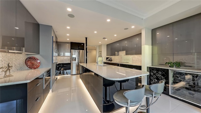 kitchen featuring gray cabinetry, backsplash, light tile floors, a center island with sink, and stainless steel refrigerator with ice dispenser