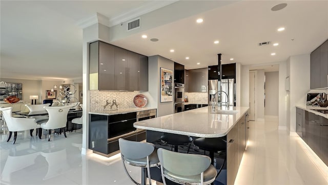 kitchen featuring light tile floors, gray cabinets, backsplash, a breakfast bar area, and a center island with sink