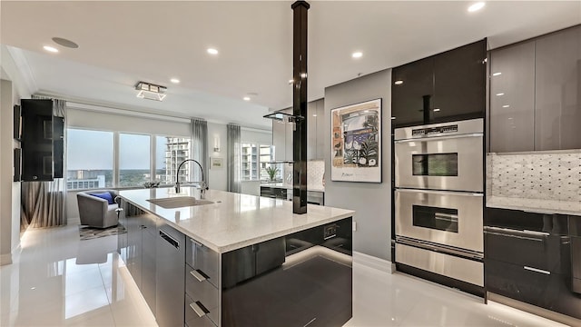 kitchen featuring an island with sink, stainless steel appliances, light tile flooring, light stone counters, and sink