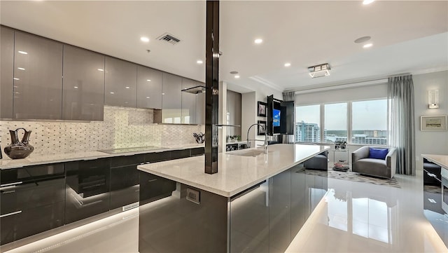 kitchen featuring light tile floors, light stone countertops, backsplash, a kitchen island with sink, and sink