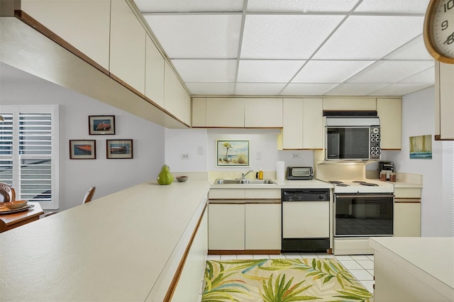 kitchen featuring a drop ceiling, white appliances, sink, cream cabinets, and light tile patterned flooring