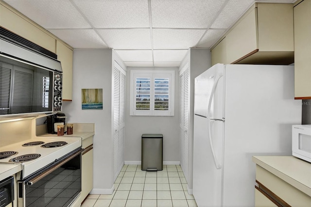 kitchen featuring a drop ceiling, white appliances, light tile patterned floors, and cream cabinets