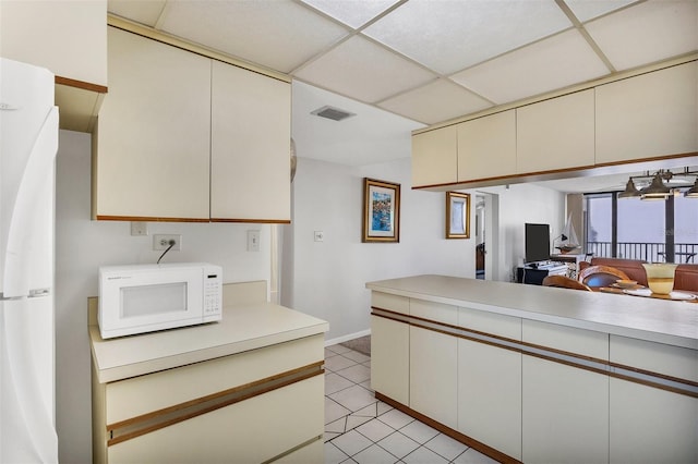 kitchen with a paneled ceiling, cream cabinets, light tile patterned floors, and white appliances