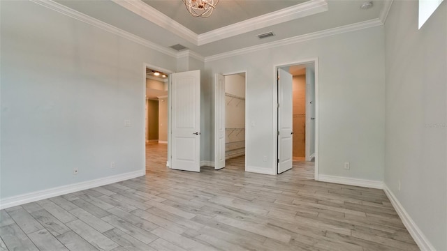 unfurnished bedroom with a closet, crown molding, a spacious closet, and light wood-type flooring