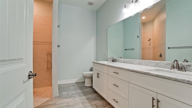 bathroom featuring a tile shower, hardwood / wood-style floors, vanity, and toilet