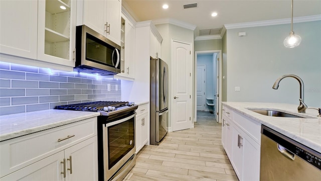 kitchen featuring stainless steel appliances, crown molding, sink, white cabinets, and light stone counters