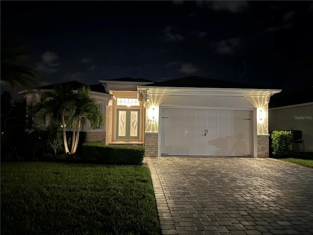 view of front of home featuring a garage, stone siding, a lawn, and decorative driveway