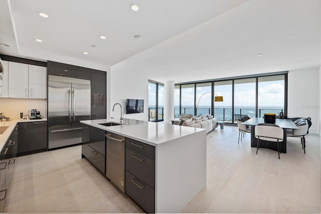 kitchen with appliances with stainless steel finishes, white cabinets, a healthy amount of sunlight, a kitchen island with sink, and sink