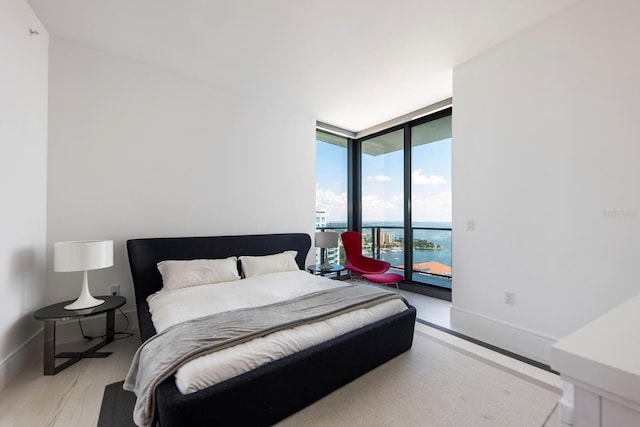 bedroom featuring a water view, access to exterior, light hardwood / wood-style floors, and a wall of windows