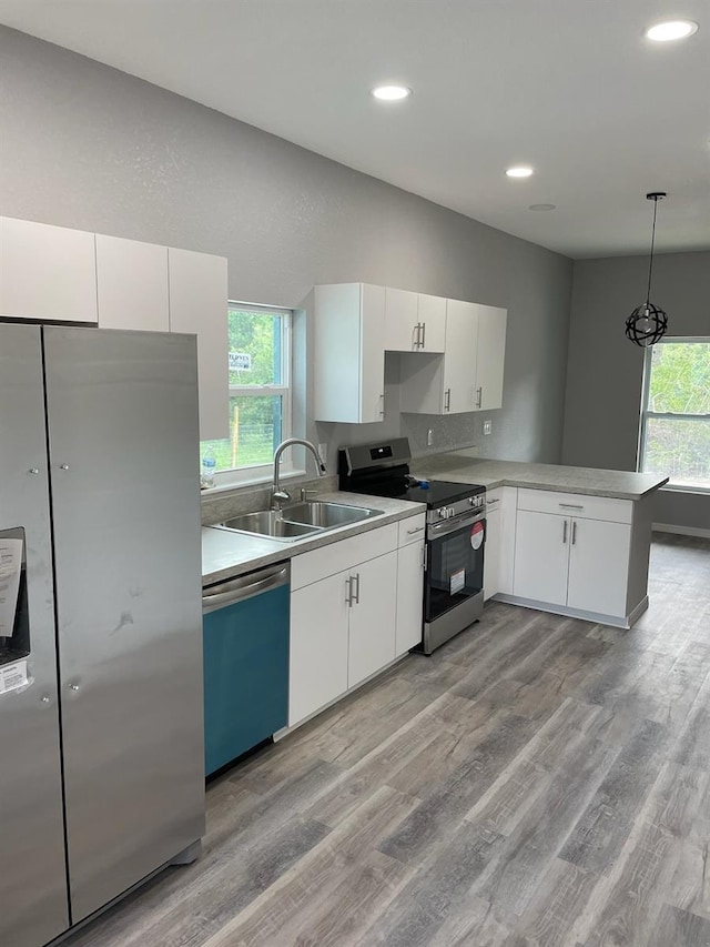 kitchen featuring light wood-type flooring, pendant lighting, white cabinetry, sink, and appliances with stainless steel finishes