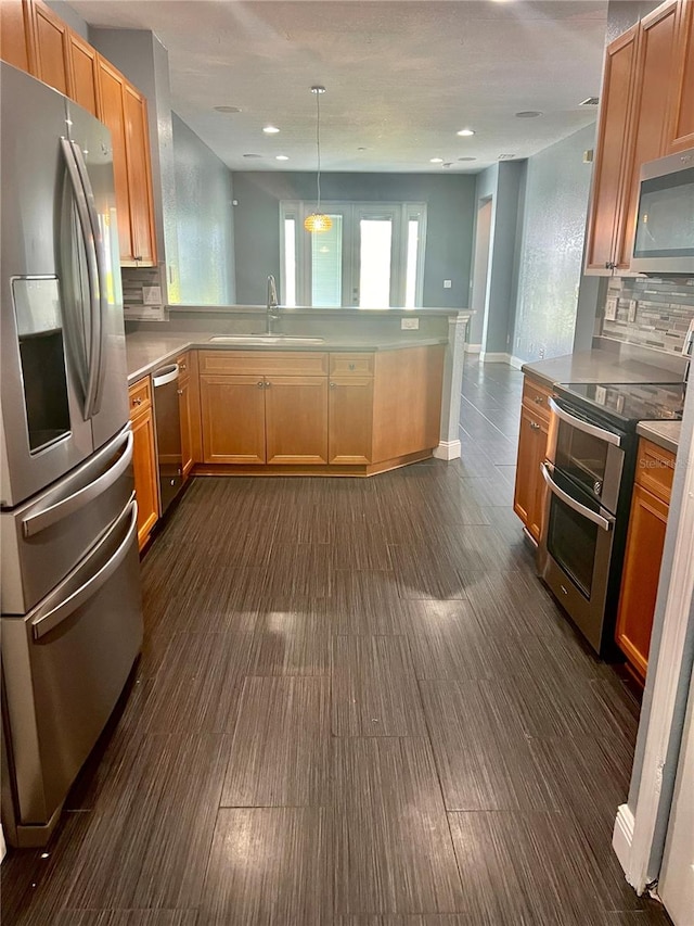 kitchen with decorative light fixtures, kitchen peninsula, appliances with stainless steel finishes, backsplash, and sink