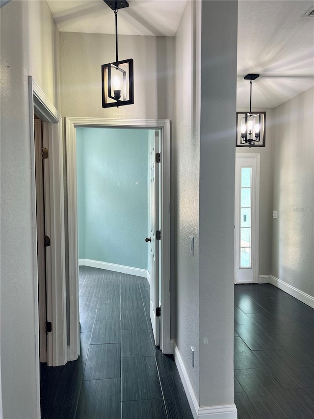 hallway with dark tile flooring and an inviting chandelier