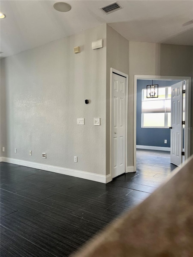 spare room featuring dark wood-type flooring and a chandelier