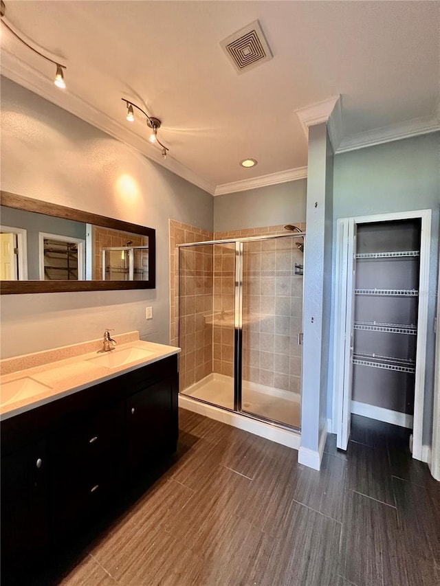 bathroom featuring an enclosed shower, double vanity, crown molding, and track lighting