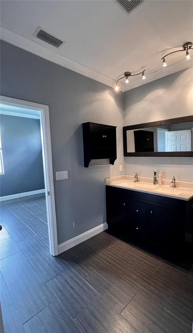 bathroom featuring vanity with extensive cabinet space, dual sinks, ornamental molding, and track lighting