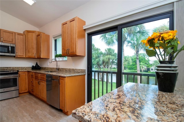 kitchen with appliances with stainless steel finishes, vaulted ceiling, light stone counters, light wood-type flooring, and sink