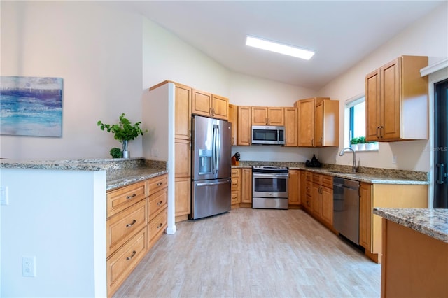 kitchen featuring lofted ceiling, stainless steel appliances, a sink, light wood-type flooring, and light stone countertops