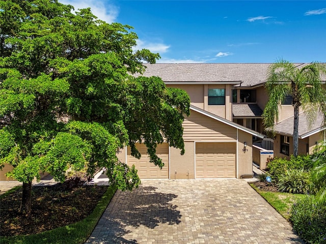 view of front facade with a garage, roof with shingles, decorative driveway, and stucco siding