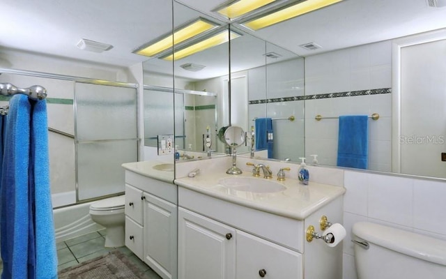 full bathroom featuring tile walls, oversized vanity, toilet, tile flooring, and bath / shower combo with glass door