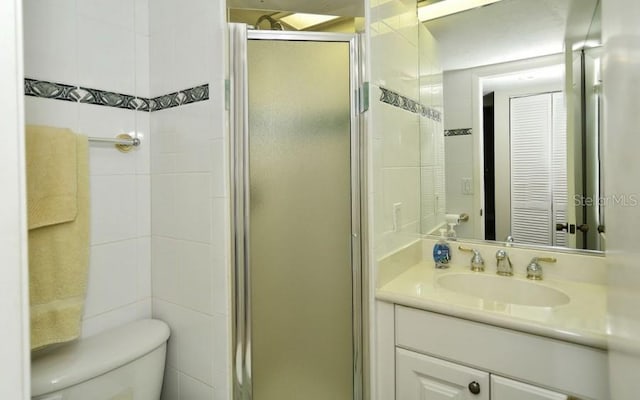 bathroom featuring tile walls, walk in shower, toilet, and vanity with extensive cabinet space